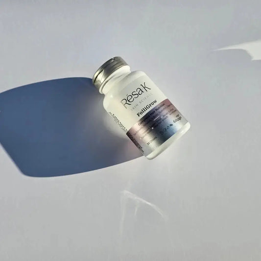 A small frosted glass vial bottle with a silver cap and a gradient label reading Resak and Fishigrow, photographed on a light gray surface with a strong blue shadow.