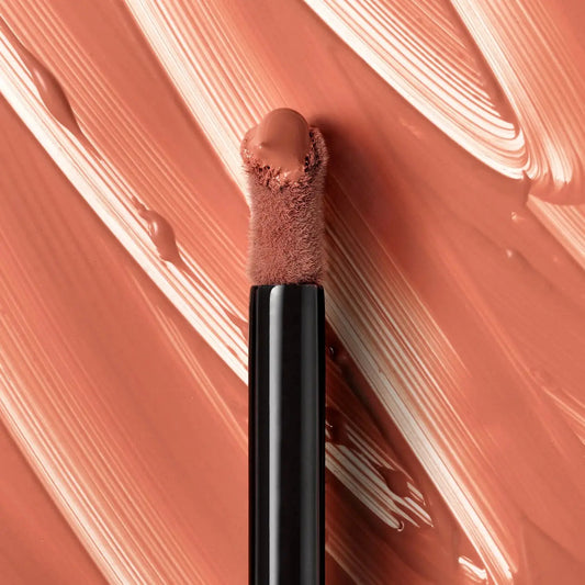 Makeup brush with beige cream on a swatch of the same color
