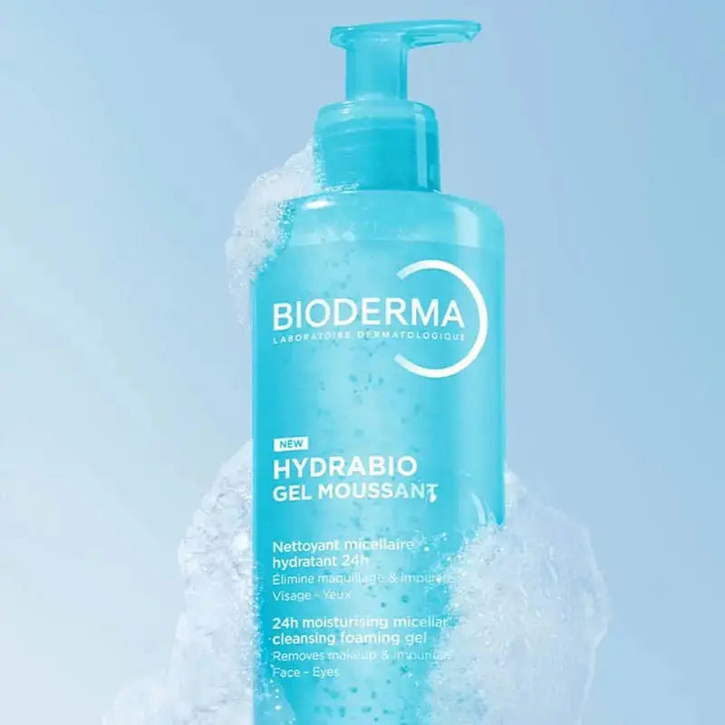 A bottle of Bioderma Hydrabio Gel Moussant cleansing foam in a translucent light blue bottle, surrounded by white foam bubbles against a soft light blue background.
