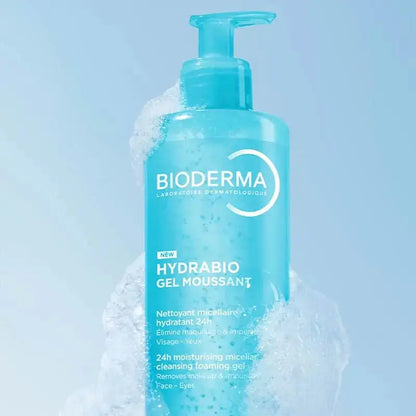A bottle of Bioderma Hydrabio Gel Moussant cleansing foam in a translucent light blue bottle, surrounded by white foam bubbles against a soft light blue background.