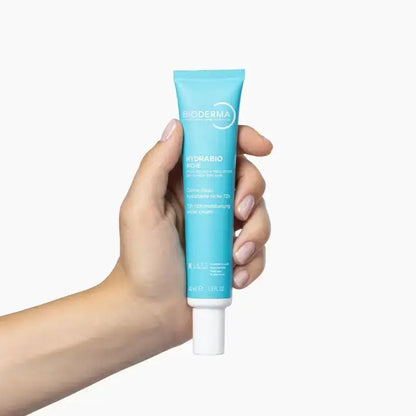 A hand holding a tube of Bioderma Rho-Coupe Hydrabio Rose skincare cream against a plain white background.