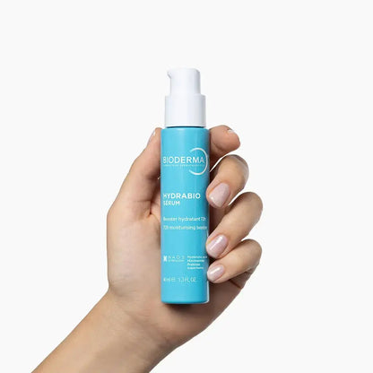 A hand holding a light blue pump bottle of Bioderma Hydrabio Serum against a clean white background.