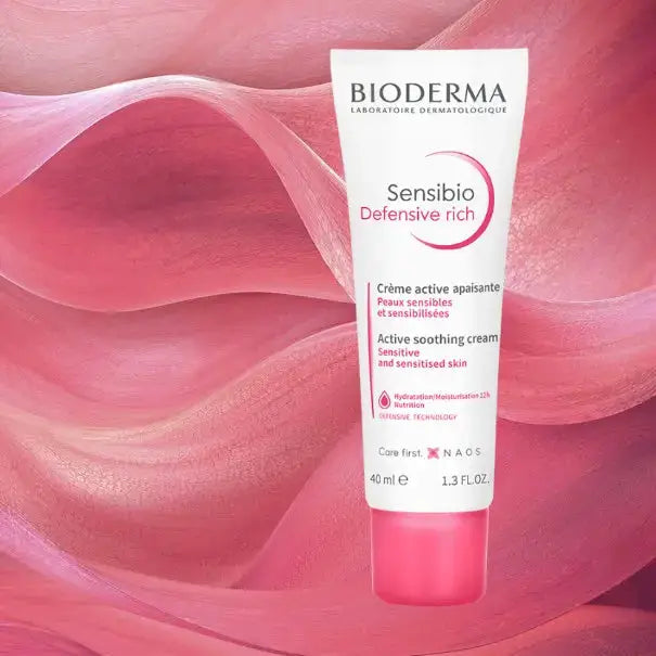 Bioderma Sensibio Defensive Rich Active Soothing Cream in a white squeeze tube with a pink cap, set against a flowing pink abstract background.