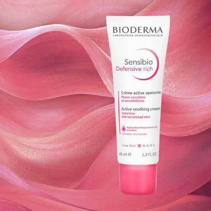 Bioderma Sensibio Defensive Rich Active Soothing Cream in a white squeeze tube with a pink cap, set against a flowing pink abstract background.