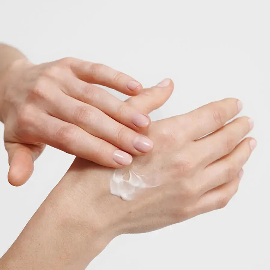 Hand applying cream to another hand on a light background