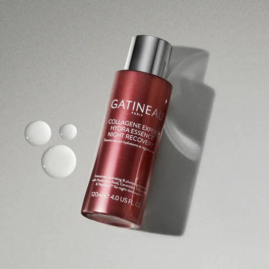 A bottle of Gatineau Paris Collagen Express Night Recovery Hydra Essence, shown at an angle on a textured gray background with three clear liquid droplets on the left.