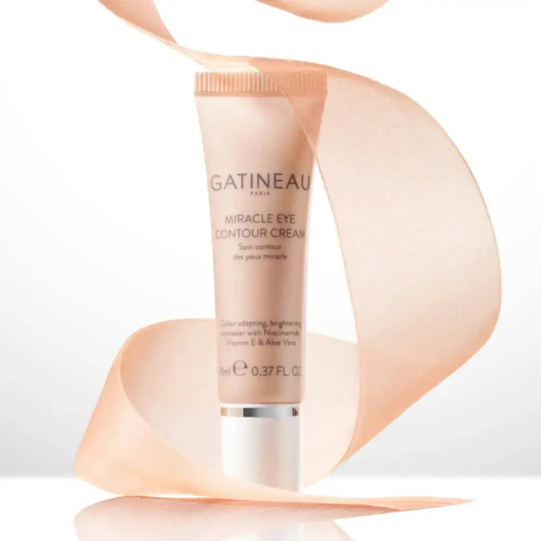 Gatineau Paris Miracle Eye Contour Cream in a peach-colored squeeze tube with a white cap, styled with a flowing peach ribbon on a white background.