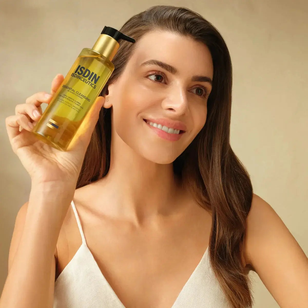 Woman holding a bottle of Isdin product against a beige background