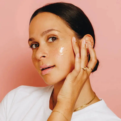 Woman applying cream to her face with a pink background