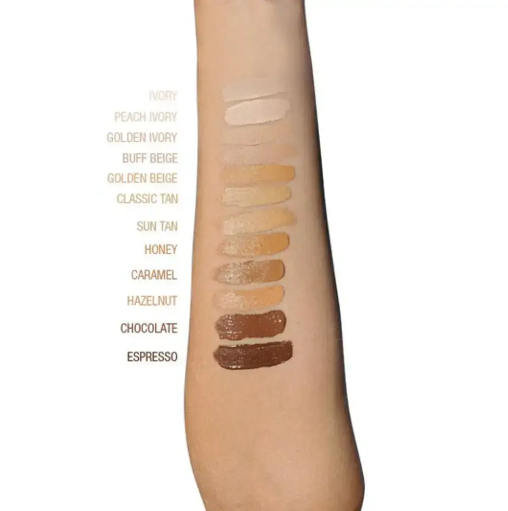 A vertical swatch strip on a person's forearm showing multiple beige, tan, and brown makeup shades with labeled names including Ivory, Peach Ivory, Golden Ivory, Buff Beige, Classic Tan, Sun Tan, Honey, Caramel, Hazelnut, Chocolate, and Espresso, on a white background.
