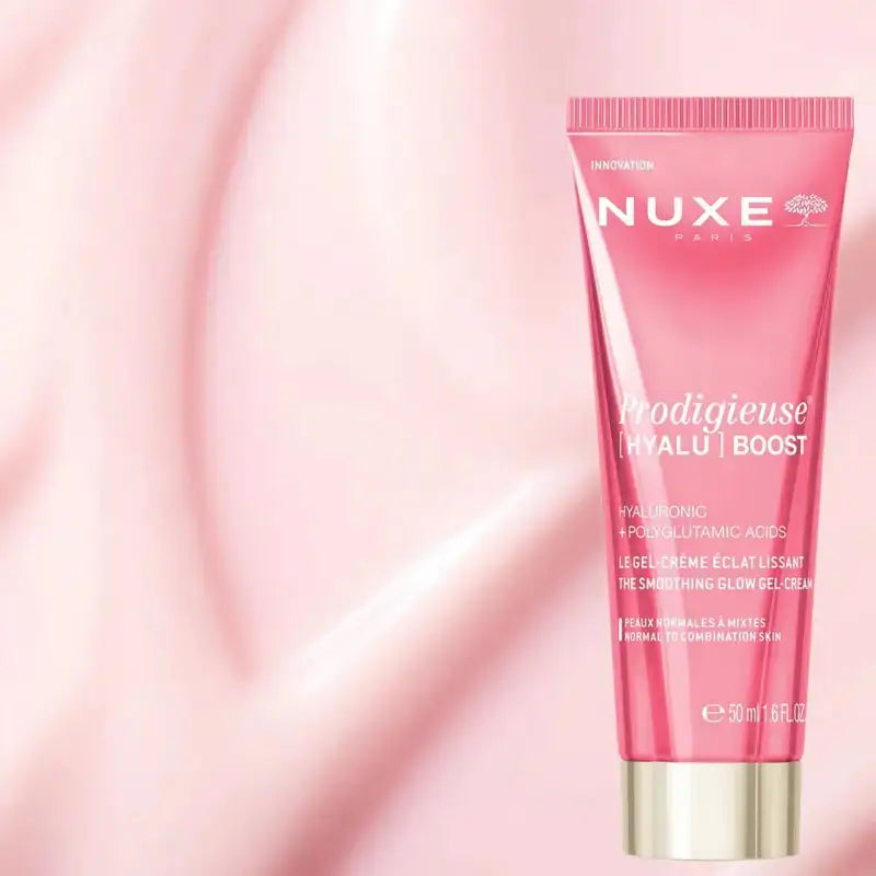 Nuxe Paris Prodigieuse Hyalu Boost eye cream in a pink squeeze tube with a metallic gold cap, set against a soft, abstract pink background.
