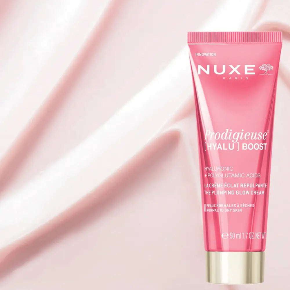 Nuxe Paris Prodigieuse [Hyalu] Boost plumping glow cream in a pink squeeze tube with a gold cap, set against a soft pink satin background.
