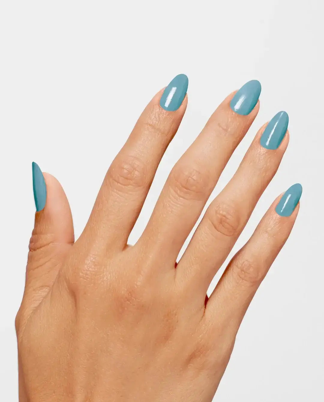 A close-up of a hand with manicured fingernails painted in a glossy dusty blue shade, set against a solid light gray background.