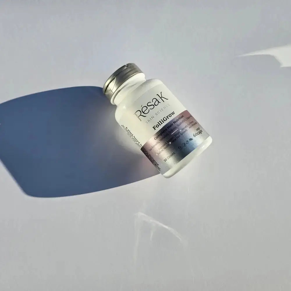 A small frosted glass vial bottle with a silver cap and a gradient label reading Resak and Fishigrow, photographed on a light gray surface with a strong blue shadow.