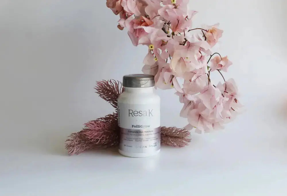 A white bottle of ResaK Polishing cream with a silver cap, styled on a white surface with pink flowers and dried brown grasses against a white background.