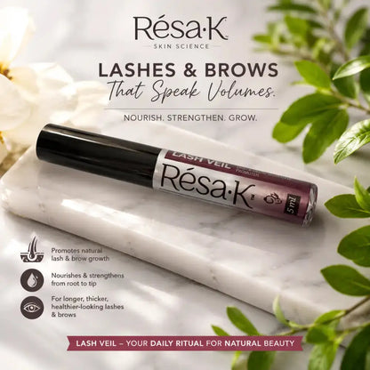 Résa-K Lash Veil 5ml lash and brow serum in a black tube with a white and purple label, resting on a white marble slab with green leaves and white flowers in the background.