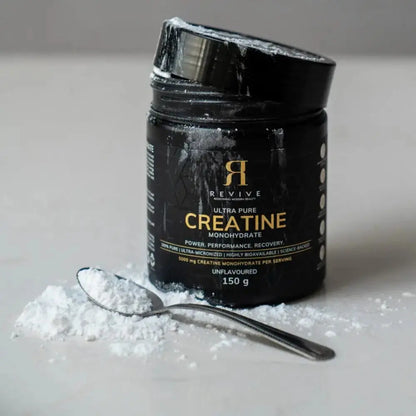 Black container of Revive Ultra Pure Creatine Monohydrate with a spoonful of powder on a light surface.