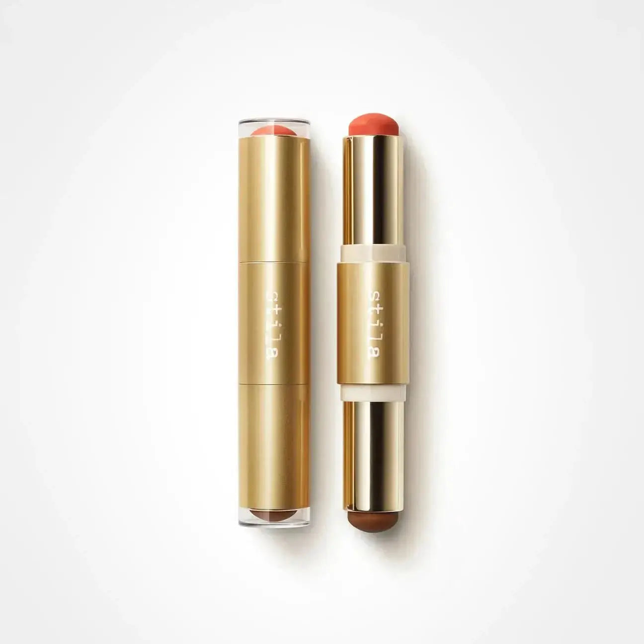 Two gold cosmetic tubes with clear caps, one closed and one open showing a coral-red stick and a brown stick, on a white background. The brand name 'dli la' is printed vertically on the tubes.