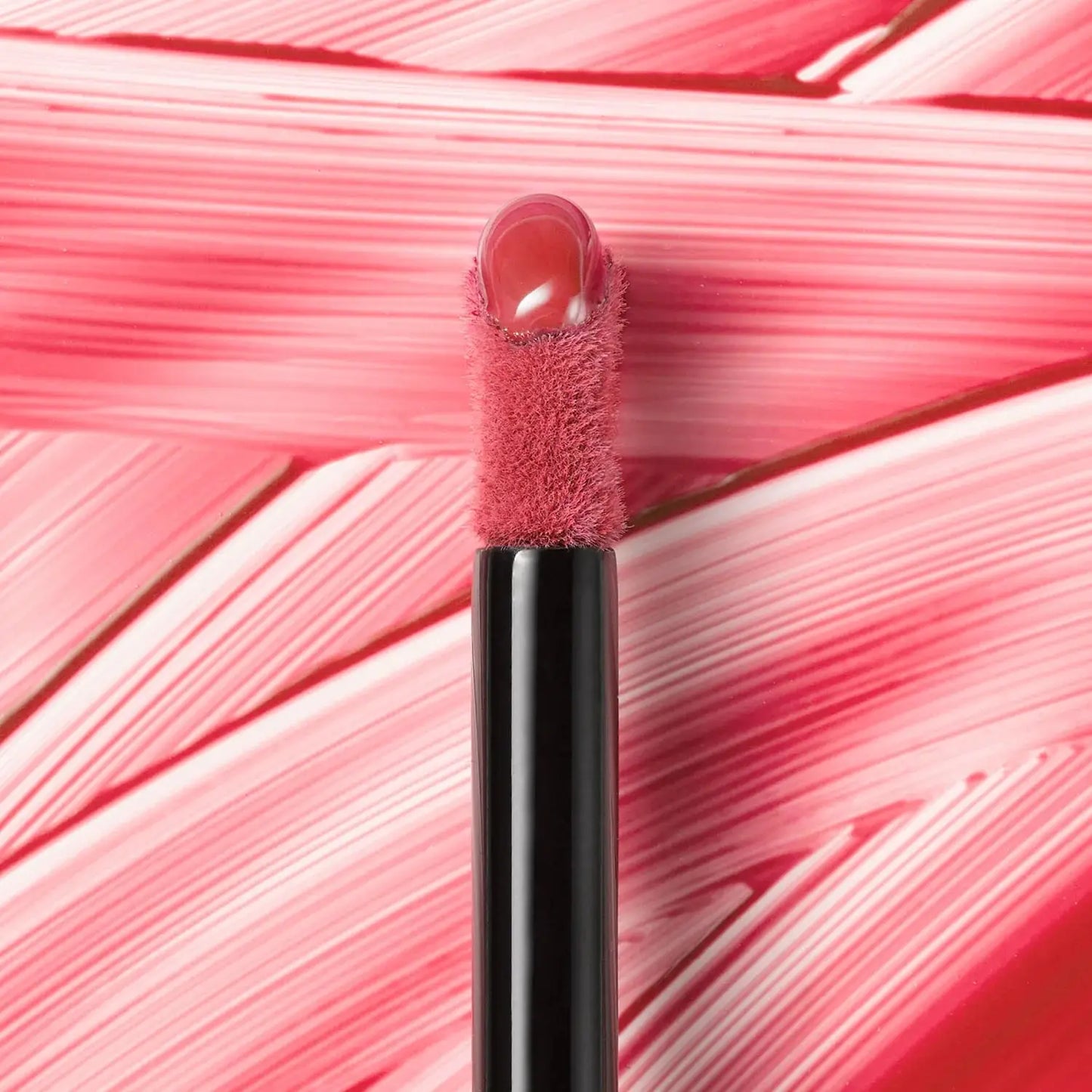 Lip gloss applicator with pink lip gloss on a pink textured background