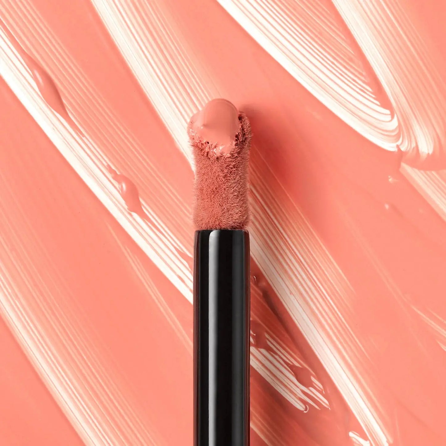 Lip brush with pink lip product on a pink and white abstract background