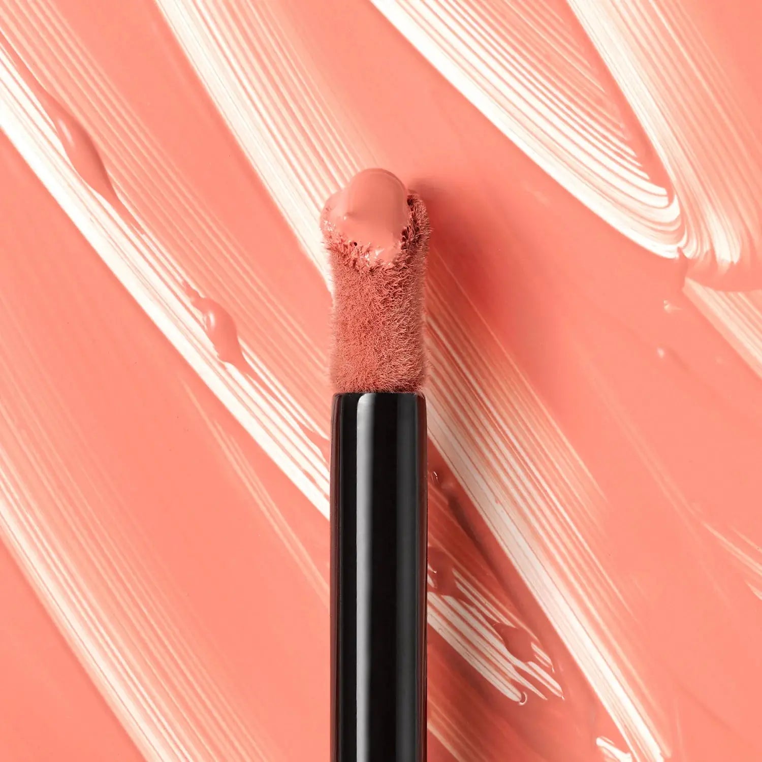 Lip brush with pink lip product on a pink and white abstract background