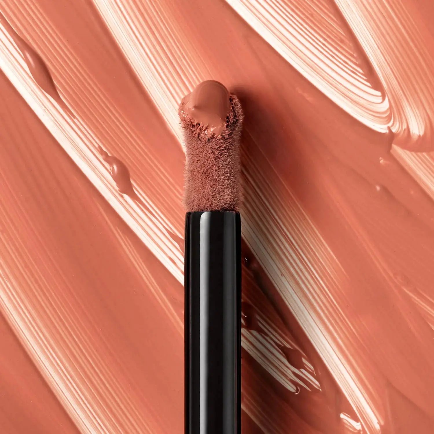 Makeup brush with beige cream on a swatch of the same color