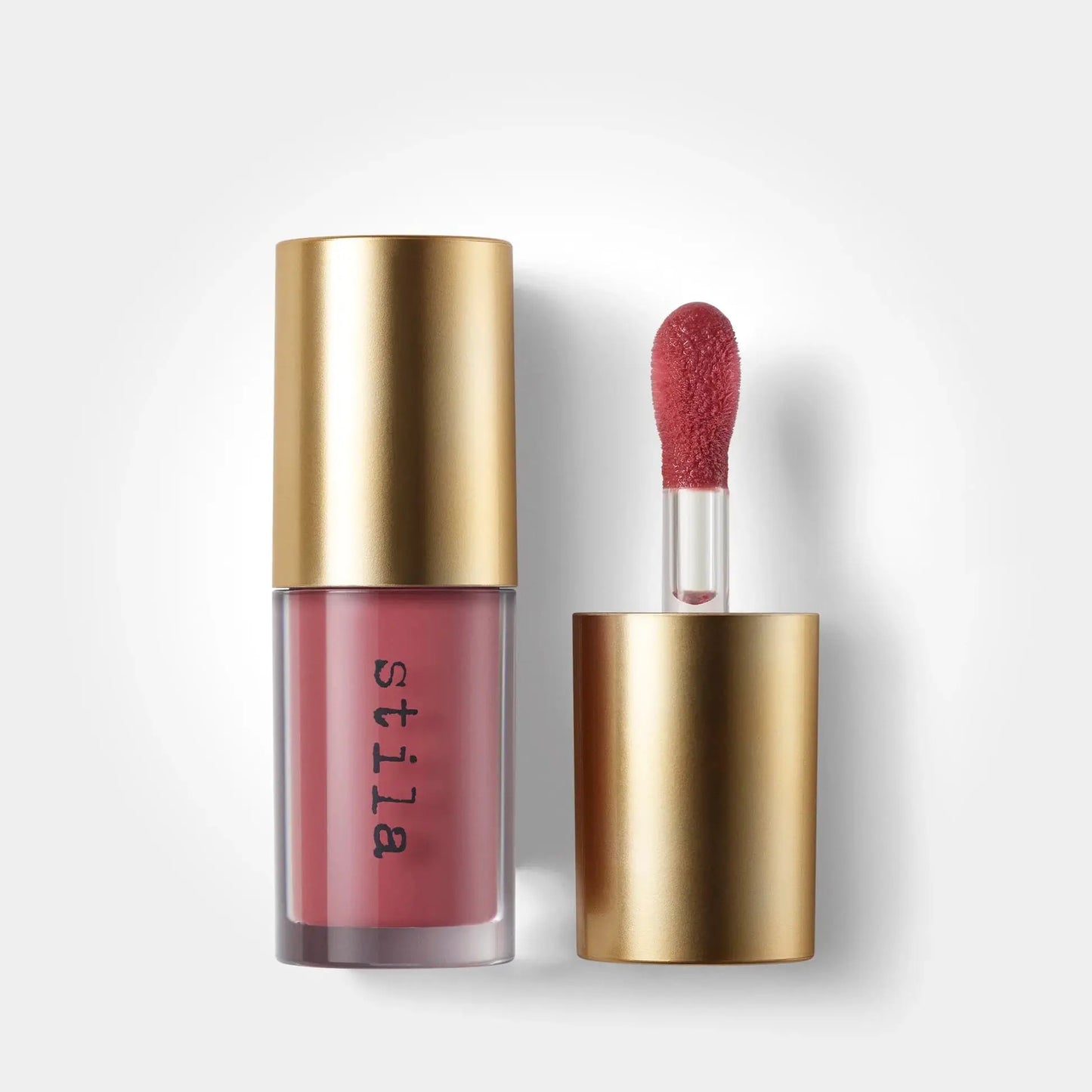 Stüla liquid lipstick in a dusty rose pink shade with a metallic gold cap, shown next to its applicator wand on a clean white background.