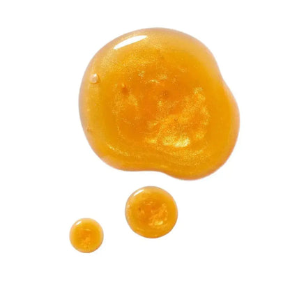 A glossy, shimmering golden-amber liquid cosmetic or gel shown as one large irregular blob with two smaller droplets below, isolated on a white background.