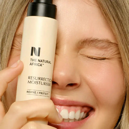 Person holding a bottle of 'The Natural Africa' Resurrection Moisturiser close to their face.