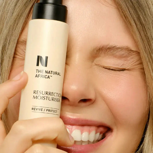 Person holding a bottle of 'The Natural Africa' Resurrection Moisturiser close to their face.